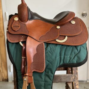 A saddle is sitting on the ground in front of a green blanket.