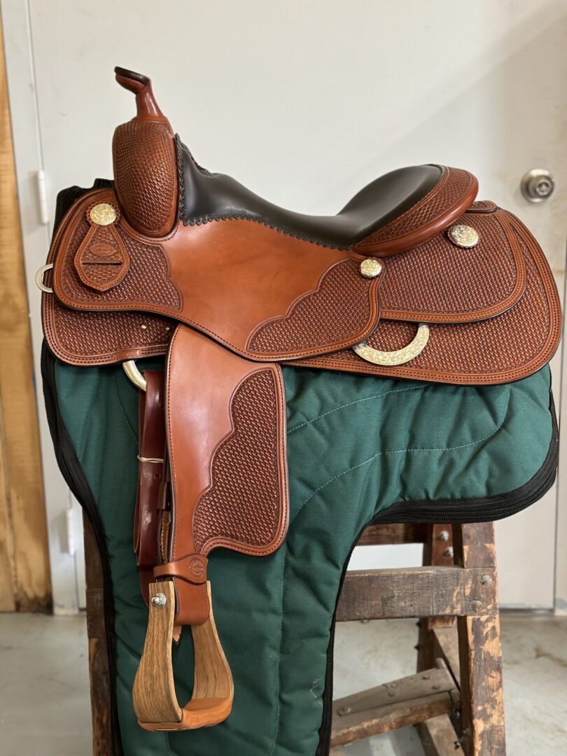 A saddle is sitting on the ground in front of a green blanket.