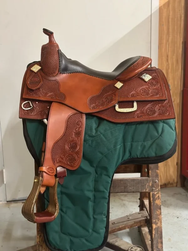 A saddle is sitting on the ground in front of a green wall.